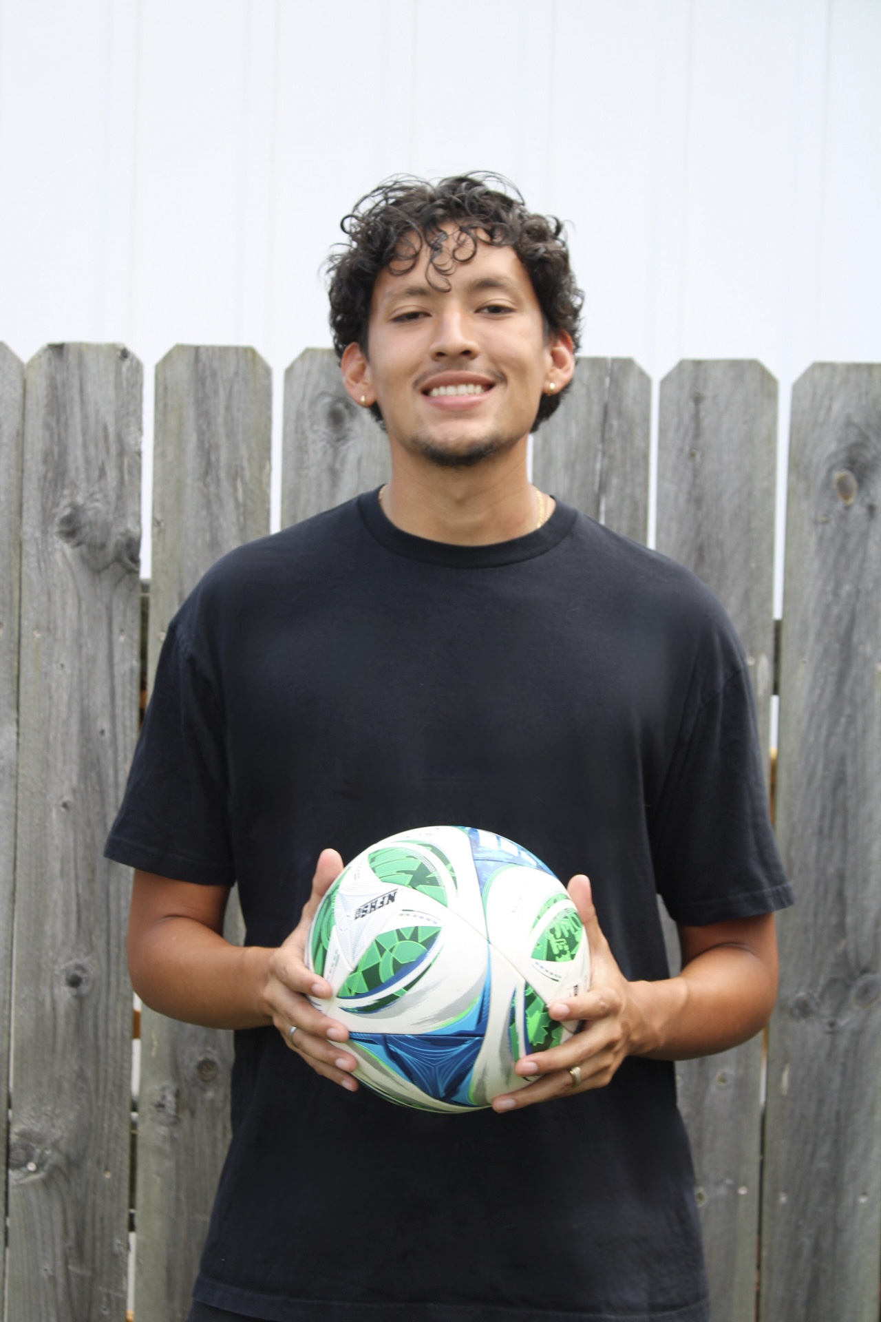 Coach Alex smiling while holding a soccer ball